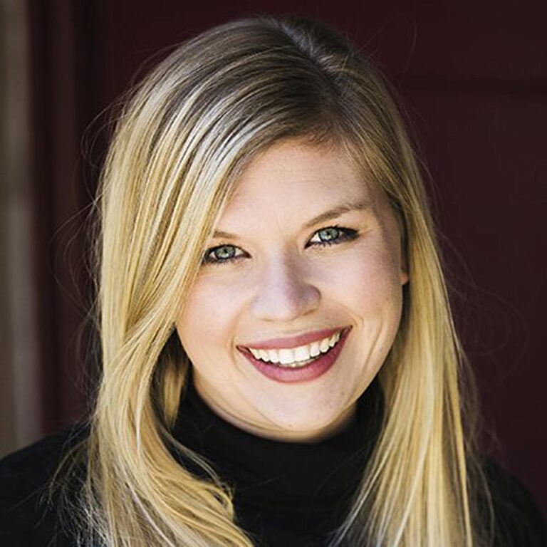 The image shows a person with long, straight blonde hair. The background appears to be a dark red or maroon color.