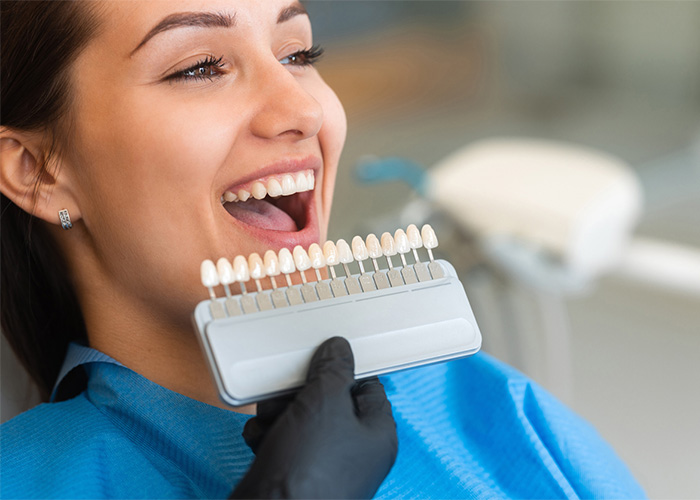 Woman in a dental clinic with a shade guide next to their mouth, showing tooth-colored tabs for matching dental restorations.